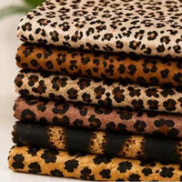 A stack of folded Leopard Print Chiffon Fabric By The Yard featuring various leopard patterns in different color combinations.