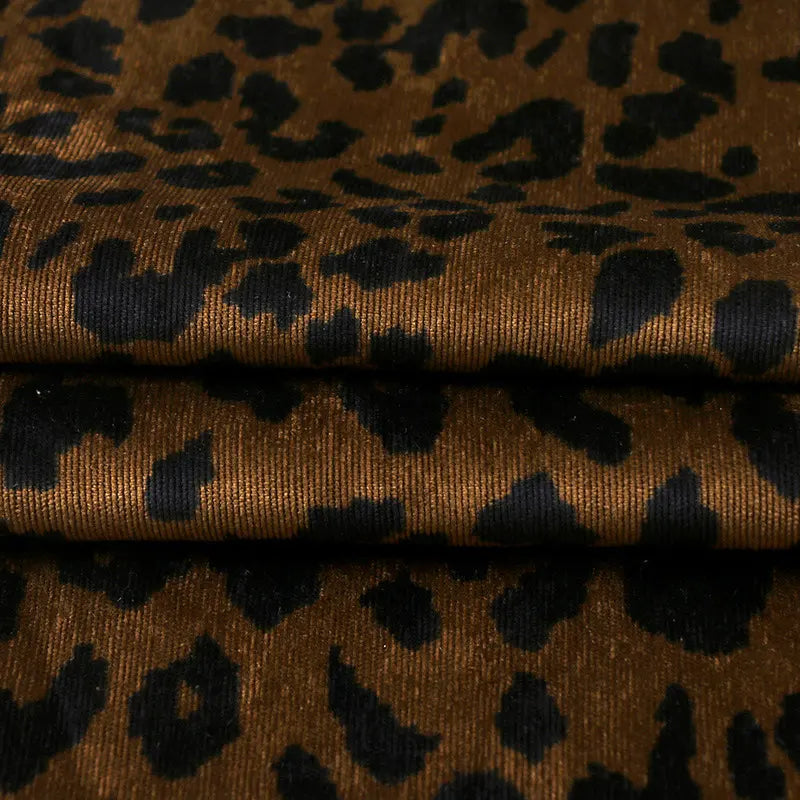 A close-up of Longan Craft's Leopard Print Corduroy Fabric by the yard shows soft, slightly shiny multicolor material with bold black spots—ideal for kids' clothing and fashion projects.
