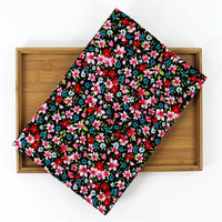 A piece of Longan Craft’s Lily Printed Cotton Corduroy Fabric—fine wale with red, pink, blue, and white floral prints on black—is displayed on a wooden tray against a white background.