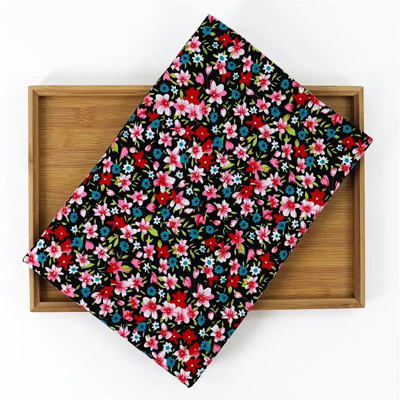 A piece of Longan Craft’s Lily Printed Cotton Corduroy Fabric—fine wale with red, pink, blue, and white floral prints on black—is displayed on a wooden tray against a white background.