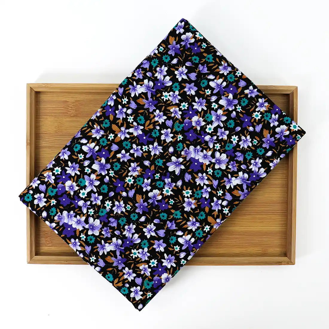 A folded piece of Lily Printed Cotton Corduroy Fabric By The Yard from Longan Craft, featuring a vibrant blue, purple, and brown floral design, rests on a wooden tray against a white background.