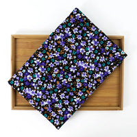 A folded piece of Lily Printed Cotton Corduroy Fabric By The Yard from Longan Craft, featuring a vibrant blue, purple, and brown floral design, rests on a wooden tray against a white background.