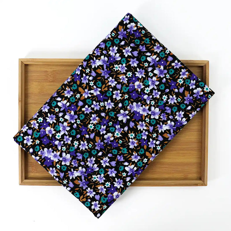A folded piece of Lily Printed Cotton Corduroy Fabric By The Yard from Longan Craft, featuring a vibrant blue, purple, and brown floral design, rests on a wooden tray against a white background.