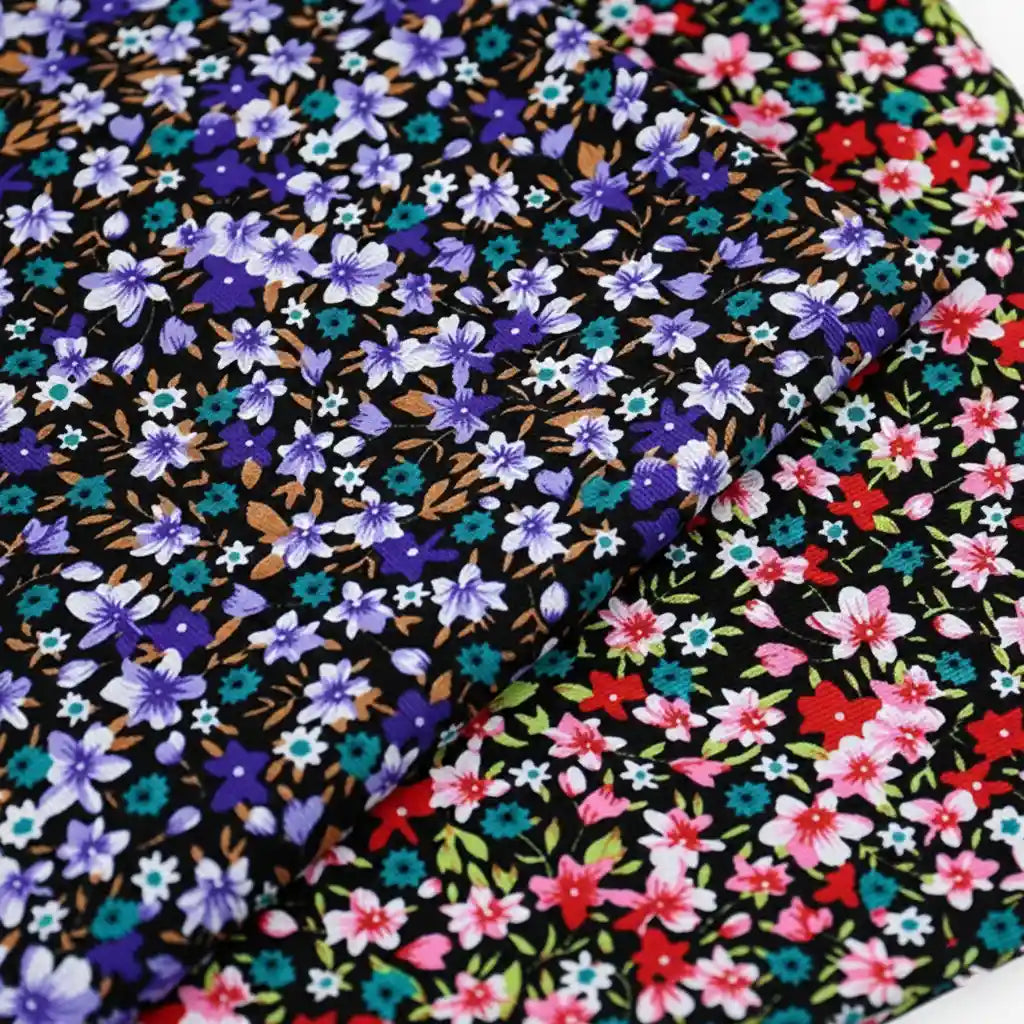 Two pieces of Longan Craft's Lily Printed Cotton Corduroy Fabric—fine wale black corduroy with dense floral prints: one with blue and purple flowers, the other featuring red, pink, turquoise blooms, and green leaves.