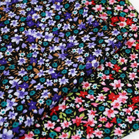 Two pieces of Longan Craft's Lily Printed Cotton Corduroy Fabric—fine wale black corduroy with dense floral prints: one with blue and purple flowers, the other featuring red, pink, turquoise blooms, and green leaves.