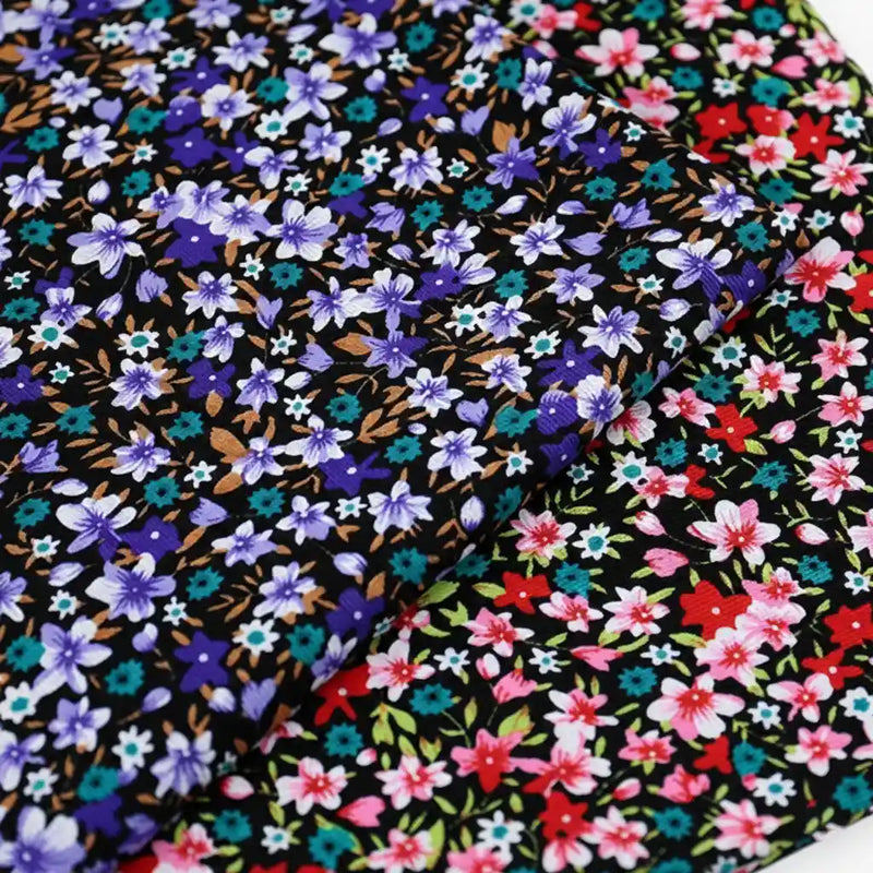 Two pieces of Longan Craft's Lily Printed Cotton Corduroy Fabric—fine wale black corduroy with dense floral prints: one with blue and purple flowers, the other featuring red, pink, turquoise blooms, and green leaves.