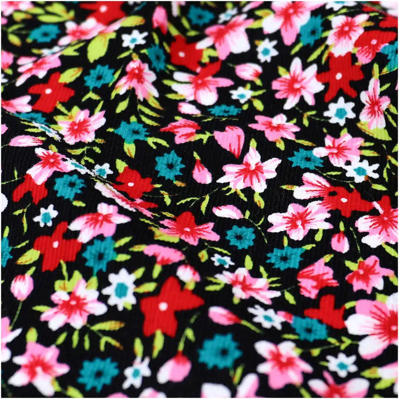Close-up of Longan Craft's Lily Printed Cotton Corduroy Fabric, featuring vibrant red, pink, blue, and green floral patterns on black fine wale cotton corduroy with visible creases and texture—ideal for tops.