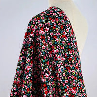 A mannequin displays the Lily Printed Cotton Corduroy Fabric by Longan Craft, featuring a fine wale corduroy with a vibrant red, pink, and white floral pattern with green leaves on a light background—ideal for tops and comfy projects.