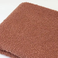 A folded piece of reddish-brown Linen Grain Boucle Fabric By The Yard with a prominent linen texture.