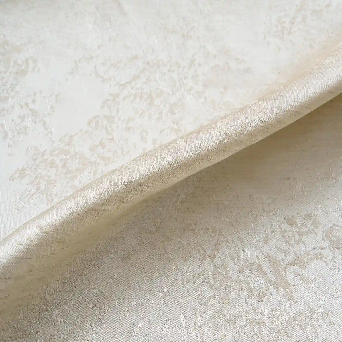 A close-up of Longan Craft’s Linen Viscose Jacquard Satin Fabric by the Yard, featuring a cream-colored, subtly shimmering floral pattern on rayon satin material, with a softly folded edge running diagonally across the image.