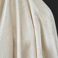 Close-up of the Linen Viscose Jacquard Satin Fabric by Longan Craft, featuring a cream-colored rayon satin material with a subtle floral pattern and luxurious textured finish, elegantly draped against a dark background.