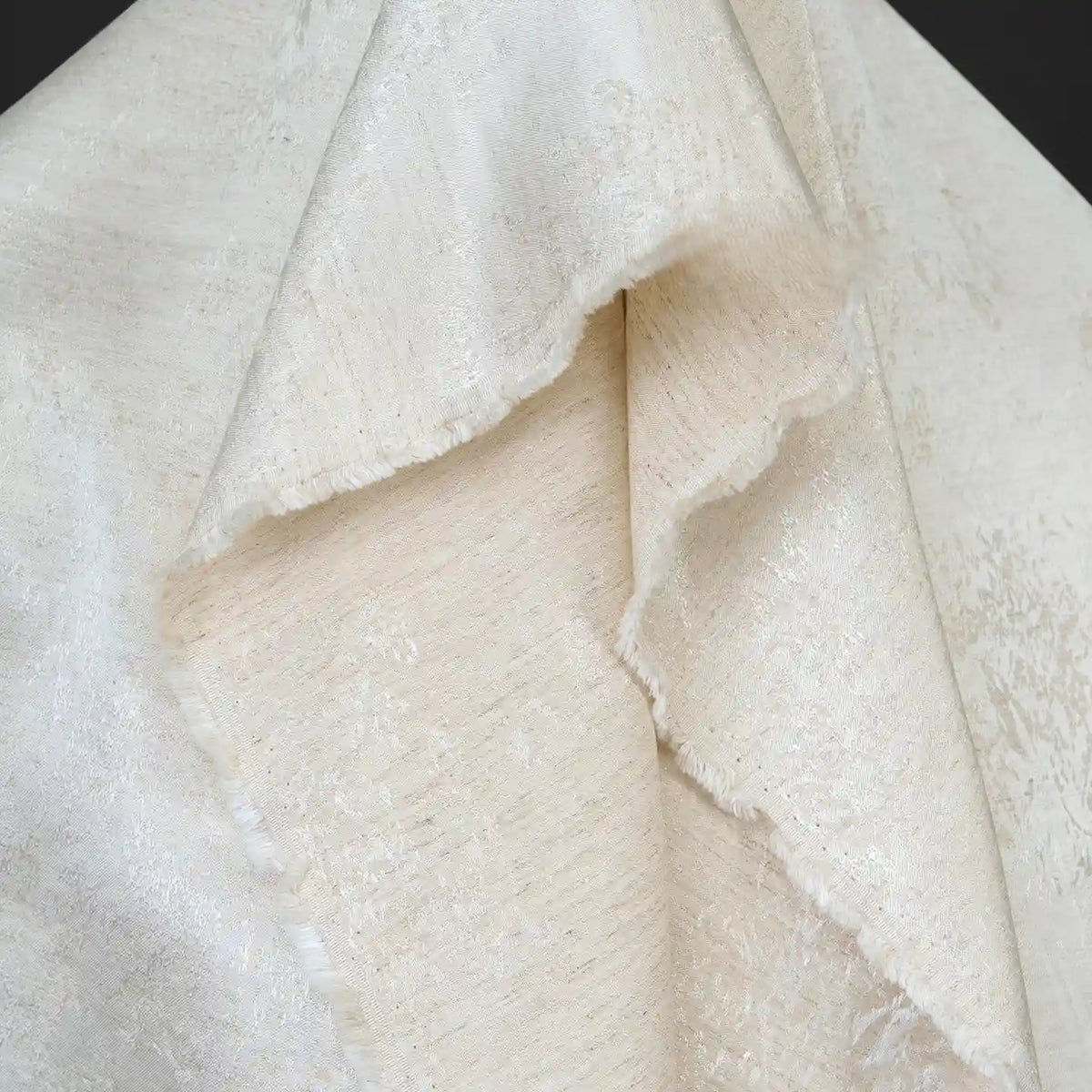 Close-up of a folded, textured off-white Linen Viscose Jacquard Satin Fabric by the yard from Longan Craft, featuring a subtle floral pattern and delicate sheen with soft, irregular edges, shown against a dark background—luxury rayon satin material perfect for dresses.