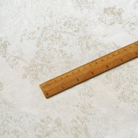 A wooden ruler marked in inches and centimeters lies diagonally across a light-colored, textured surface with subtle marbled patterns, reminiscent of the Linen Viscose Jacquard Satin Fabric by the yard from Longan Craft, featuring a subtle floral pattern and luxurious rayon satin material.