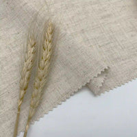 Two dried wheat stalks rest on a piece of Longan Craft’s multicolor linen and viscose fabric, ideal for summer projects, with zigzag-cut edges displayed on a plain white background.