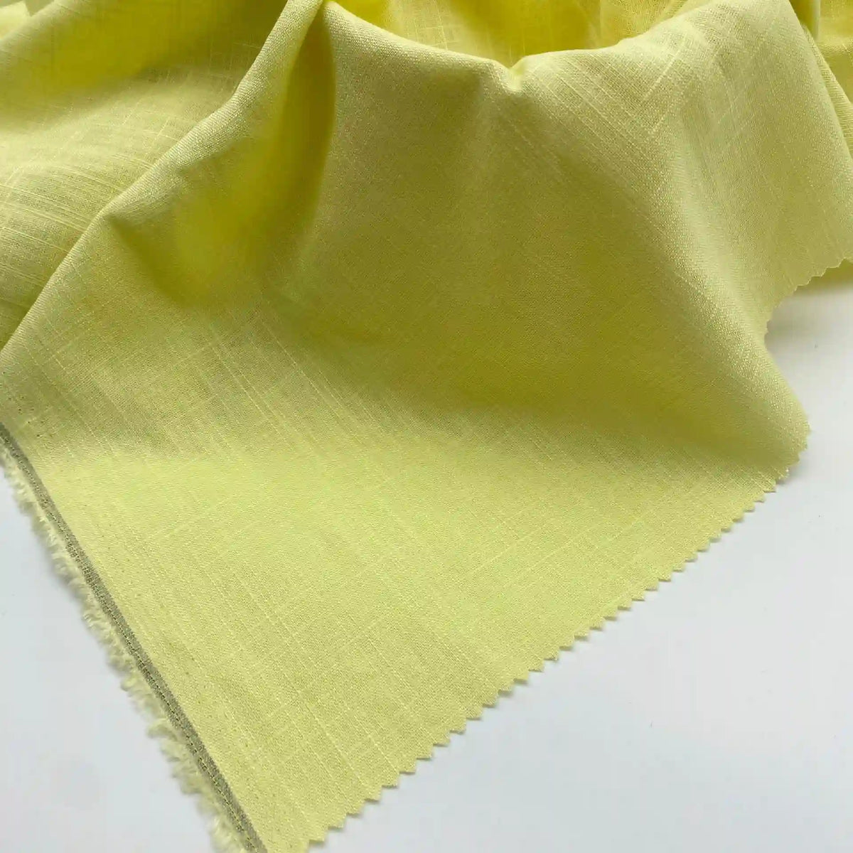 A close-up of Longan Craft's Linen and Viscose Fabric By The Yard shows its light yellow, slightly textured weave, draped loosely with a zigzag pinked edge—ideal multicolor viscose for summer from their viscose cellulose fabric collection.