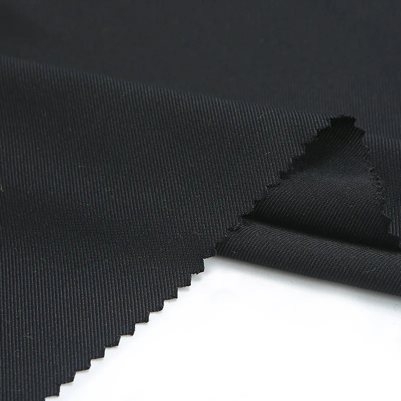 A close-up of Longan Craft’s Matte Finish Gabardine Fabric by the yard shows its durable twill weave and zigzag-cut edges, ideal for jackets, displayed on a white surface.