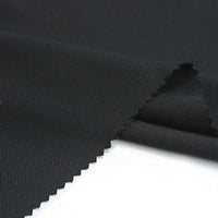 A close-up of Longan Craft’s Matte Finish Gabardine Fabric by the yard shows its durable twill weave and zigzag-cut edges, ideal for jackets, displayed on a white surface.