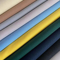 A close-up of Longan Craft's Matte Finish Gabardine Fabric by the yard shows neatly stacked twill weave rolls in beige, pink, and navy, highlighting its smooth, wrinkle-resistant texture and vibrant colors—ideal for jackets and versatile projects.