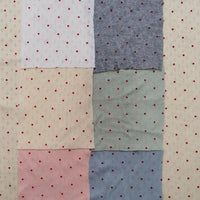 Six swatches of Mini Red Dot Printed Pointelle Fabric By The Yard in white, cream, pink, grey, green, and blue, arranged in a grid over a cream-colored red-dotted background.
