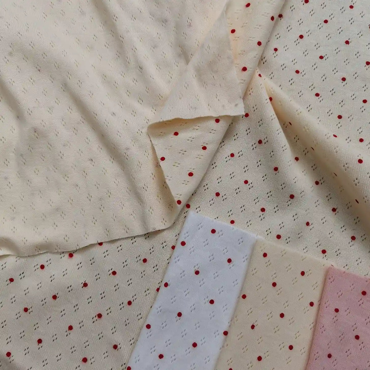 Cream-colored Mini Red Dot Printed Pointelle Fabric By The Yard shown alongside white, cream, and pink cotton jersey swatches.