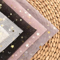 Multiple sheets of Longan Craft's Moon Star Sequins Tulle Fabric By The Yard in various colors are layered on a circular mat, perfect for infusing stage costumes with a magical, multicolor glitter effect.