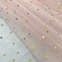 A close-up of Longan Craft’s Moon Star Sequins Tulle Fabric by the yard—multicolor glitter tulle, ideal for stage costumes—shows shiny gold star and dot sequins on pale pink tulle, laid over a white surface with gold stars.