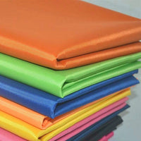 A stack of Multicolor 300D Oxford Fabric By The Yard from Longan Craft, in bright orange, green, blue, yellow, pink, and black PU coated polyester sheets, is neatly arranged on top of each other—ideal for bags and backpacks.
