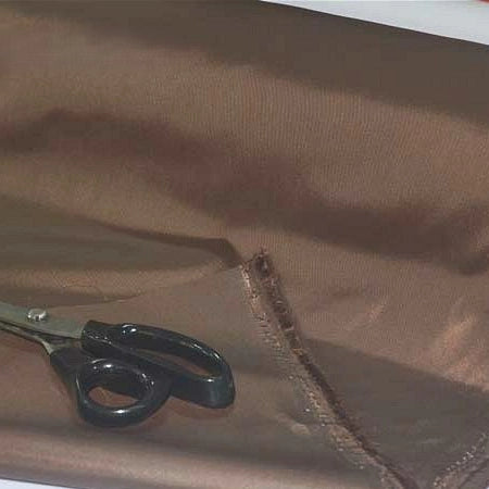 A pair of black-handled scissors rests on a piece of Longan Craft Multicolor 300D Oxford Fabric By The Yard, a durable PU coated polyester material ideal for bags and backpacks, with a rough, partially cut edge visible.