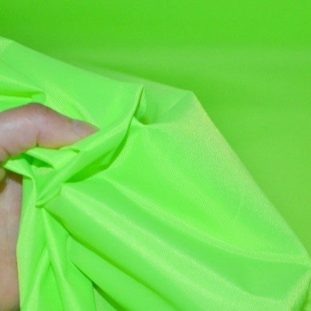 A hand holds and scrunches bright neon green Longan Craft Multicolor 300D Oxford Fabric by the yard, a durable PU coated polyester material, against a matching background—ideal for bags and backpacks.