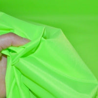 A hand holds and scrunches bright neon green Longan Craft Multicolor 300D Oxford Fabric by the yard, a durable PU coated polyester material, against a matching background—ideal for bags and backpacks.
