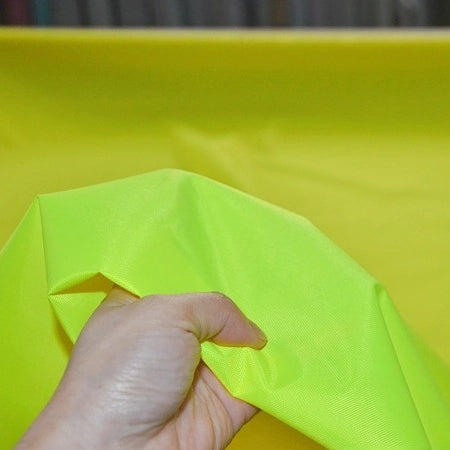 A hand holding Longan Craft's Multicolor 300D Oxford Fabric by the yard—durable, PU-coated polyester ideal for bags and backpacks—in bright yellow-green, shown against a matching background.