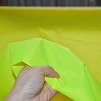 A hand holding Longan Craft's Multicolor 300D Oxford Fabric by the yard—durable, PU-coated polyester ideal for bags and backpacks—in bright yellow-green, shown against a matching background.