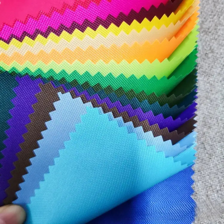 A hand displays a fan of Longan Craft’s multicolor 300D Oxford fabric swatches—PU coated, durable polyester ideal for bags and backpacks—each with pinked edges, set against a gray background.