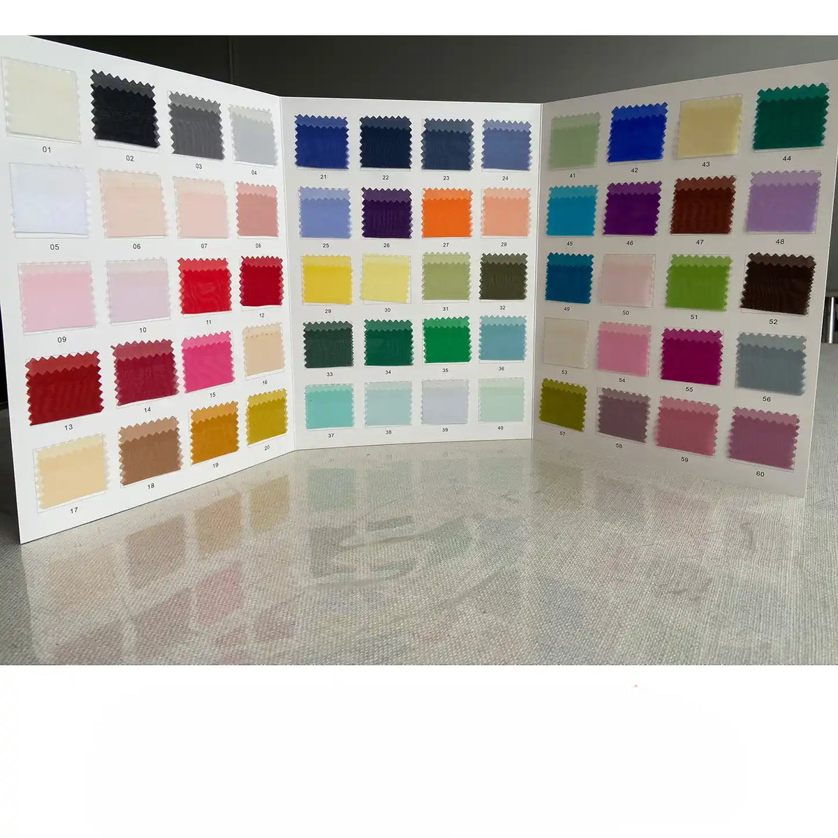 A trifold display board showcases numbered swatches of Longan Craft's Multicolor 8 Momme Organza Pure Mulberry Silk Fabric, neatly arranged in a colorful grid on a reflective surface.