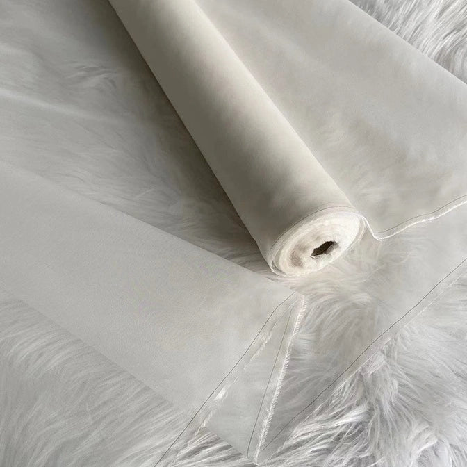 A roll of Longan Craft’s Multicolor 8 Momme Organza Silk Fabric By The Yard, made from pure mulberry silk, is displayed on a white surface, highlighting its delicate, translucent luxury—ideal for creating elegant dresses.