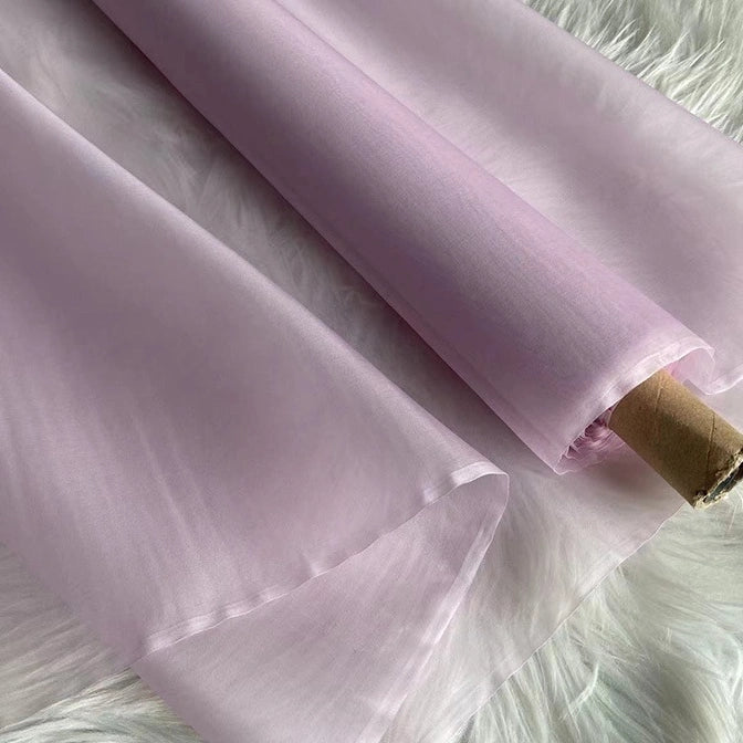 A roll of Longan Craft’s Multicolor 8 Momme Organza Silk Fabric By The Yard—sheer pure mulberry silk for luxury dresses—is partially unrolled and displayed on a fluffy white surface.