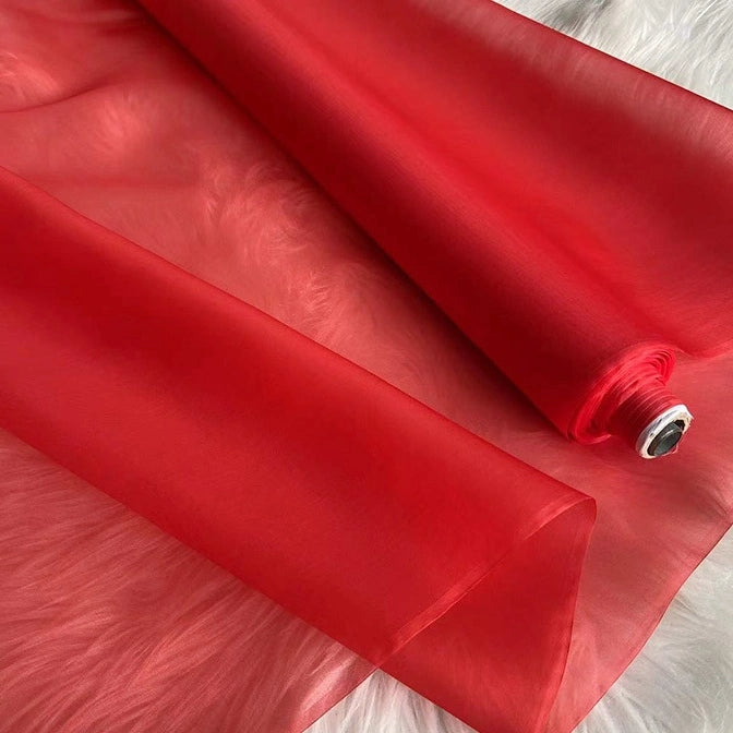 A partially unrolled yard of Longan Craft’s Multicolor 8 Momme Organza Silk Fabric—pure mulberry silk—rests on a white textured surface, highlighting its luxurious, sheer, and translucent quality for elegant dresses.