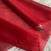 A roll of Multicolor 8 Momme Organza Silk Fabric by Longan Craft is unrolled on a soft white surface, highlighting its translucent, delicate luxury—ideal for crafting elegant dresses from pure mulberry silk by the yard.