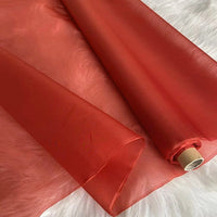 A roll of Longan Craft's Multicolor 8 Momme Organza Silk Fabric By The Yard, made from pure mulberry silk, is partially unrolled on a white furry surface. This lightweight, smooth, translucent luxury silk is ideal for elegant dresses.