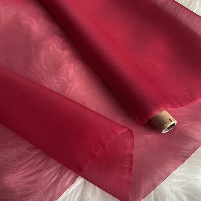 A roll of Longan Craft Multicolor 8 Momme Organza Silk Fabric By The Yard, made from pure mulberry silk, is unrolled on a white furry surface. This luxury silk has a delicate, translucent appearance and a smooth texture—ideal for dresses.