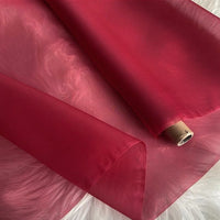 A roll of Longan Craft Multicolor 8 Momme Organza Silk Fabric By The Yard, made from pure mulberry silk, is unrolled on a white furry surface. This luxury silk has a delicate, translucent appearance and a smooth texture—ideal for dresses.