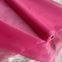 A roll of Longan Craft Multicolor 8 Momme Organza Silk Fabric By The Yard, made from pure Mulberry silk, is partially unrolled on a white textured surface. The luxury material looks lightweight, translucent, and glossy—perfect for dresses.