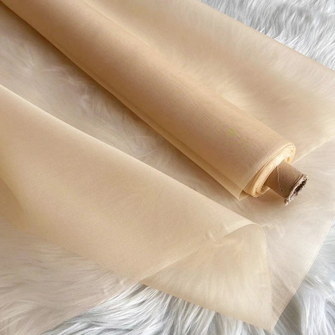 A roll of Longan Craft’s Multicolor 8 Momme Organza Silk Fabric By The Yard, made from pure mulberry silk for luxury dresses, is unrolled to reveal its sheer, delicate, and translucent texture on a textured white surface.
