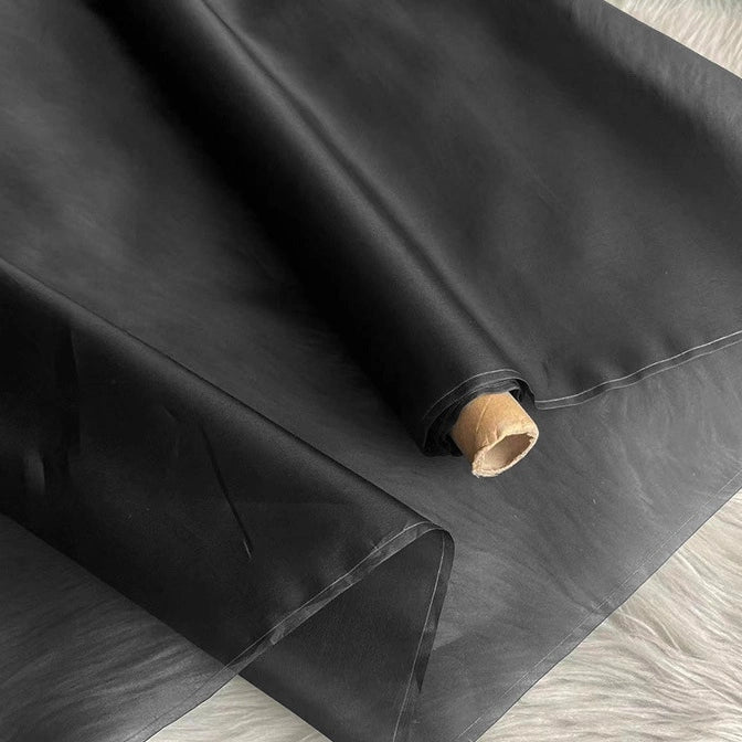 A roll of black faux leather fabric is partially unrolled, its smooth, glossy finish making it perfect to pair with Longan Craft's Multicolor 8 Momme Organza Silk Fabric By The Yard for luxury evening dresses.