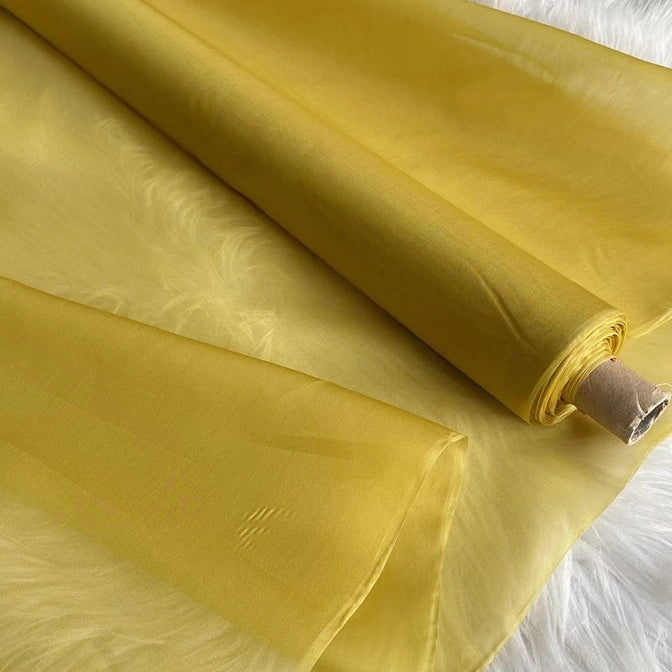 A roll of Longan Craft Multicolor 8 Momme Organza Silk Fabric, made from pure Mulberry silk and perfect for luxury dresses, is partially unrolled on a white, fluffy surface, highlighting its lightweight and translucent texture.