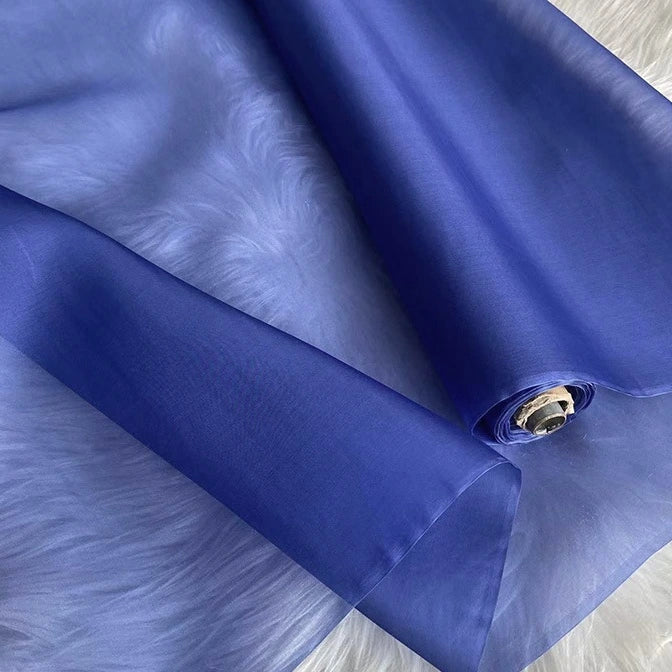 A partially unrolled yard of Longan Craft Multicolor 8 Momme Organza Silk Fabric, made from pure mulberry silk, rests on a soft white furry surface, showcasing its smooth, translucent luxury ideal for dresses.