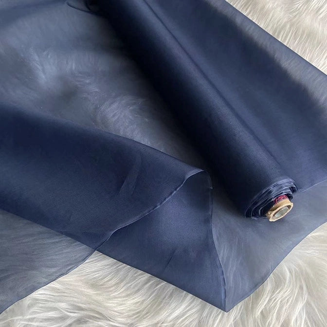 A roll of Longan Craft’s Multicolor 8 Momme Organza Silk Fabric by the yard, made from pure mulberry silk, is shown partially unrolled on a soft white surface—ideal luxury material for elegant dresses.