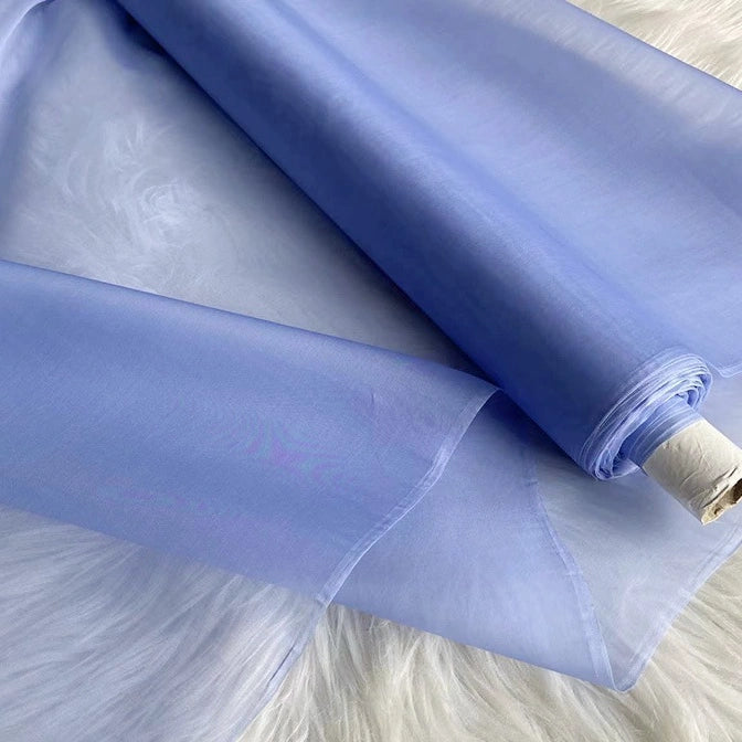 A roll of Longan Craft Multicolor 8 Momme Organza Silk Fabric By The Yard, made from pure mulberry silk, is partially unrolled on a white surface. This lightweight, sheer luxury material is perfect for elegant dresses and evening gowns.