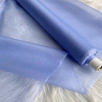 A roll of Longan Craft Multicolor 8 Momme Organza Silk Fabric By The Yard, made from pure mulberry silk, is partially unrolled on a white surface. This lightweight, sheer luxury material is perfect for elegant dresses and evening gowns.