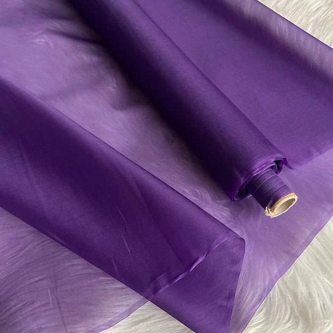 A roll of Longan Craft's Multicolor 8 Momme Organza Silk Fabric by the yard, made from pure mulberry silk, is partially unrolled to reveal its sheer, vibrant texture—ideal luxury material for making elegant dresses.